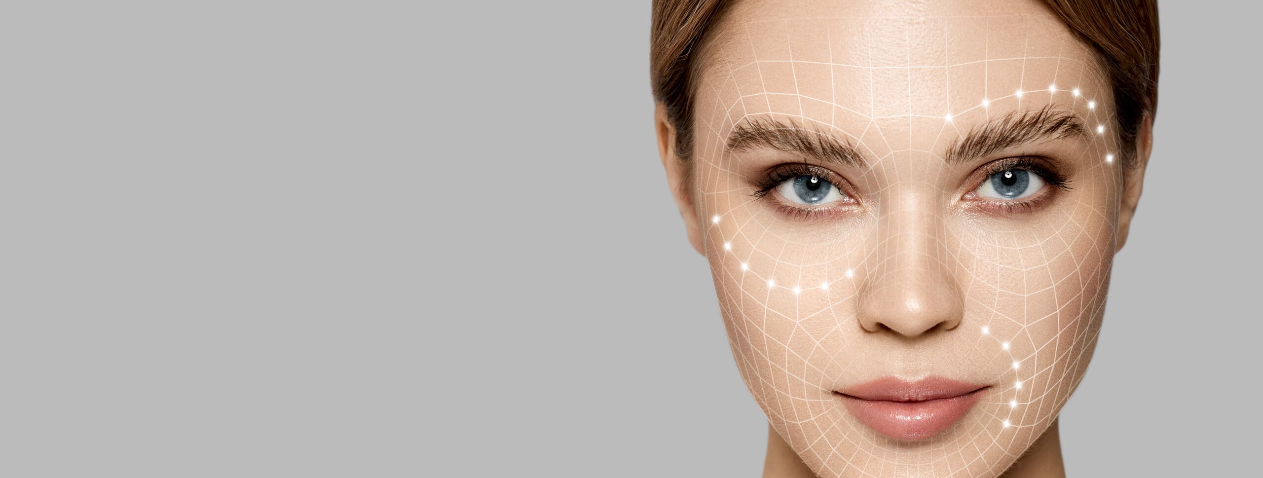 A woman’s face with a digital facial mapping grid overlay, focusing on her eyes and cheeks, on a gray background.